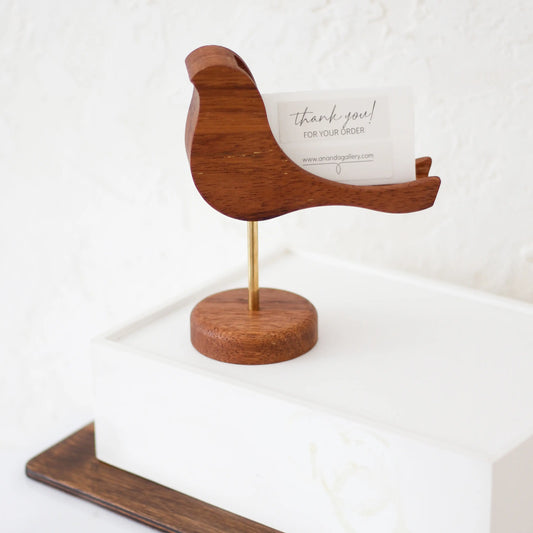 Wooden bird figurine on a round brass base with a groove for holding business cards and notes. Made from natural Iroko wood, the bird tilts slightly, adding charm to this elegant desk organizer.