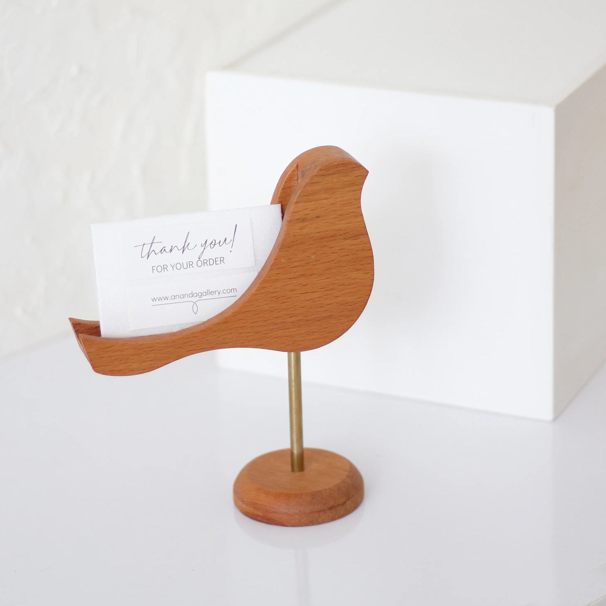 Handcrafted wooden bird perched on a brass stand with a built-in slot for business cards and memo papers. Available in Beech wood, featuring a charming tilted design perfect for office desks.